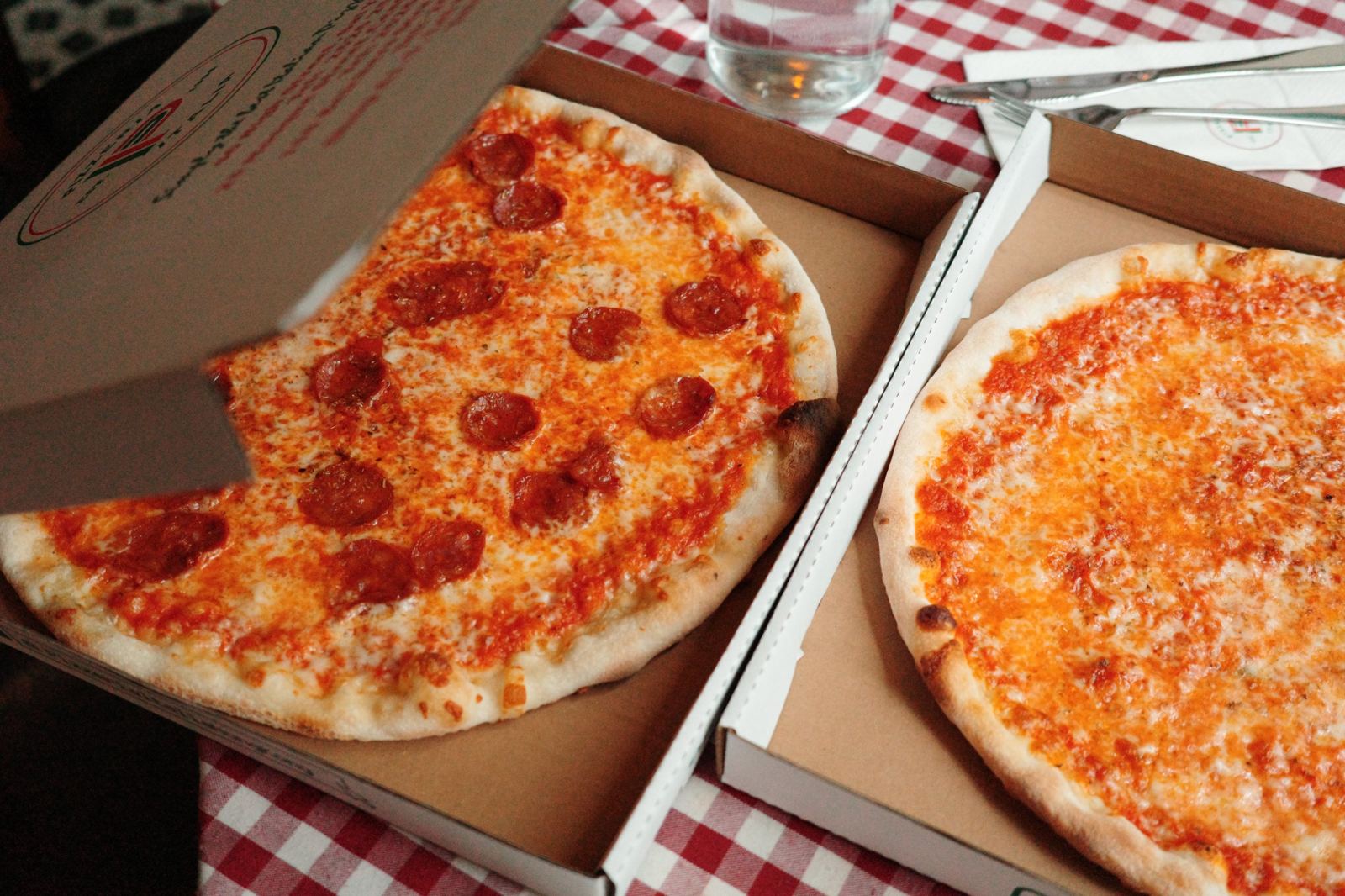 Two Pizzeria Italia pizzas in their boxes on a checked tablecloth